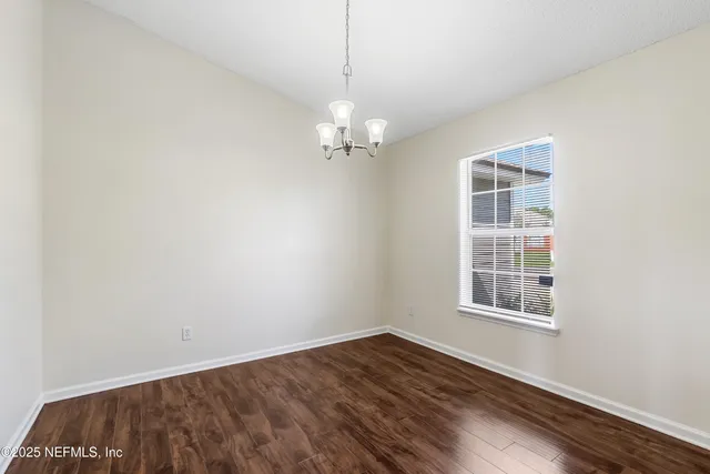 an empty room with wooden floor chandelier and windows