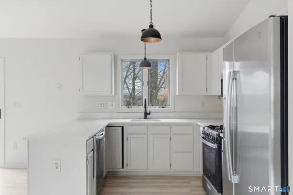 a kitchen with kitchen island granite countertop a sink stove a refrigerator and white cabinets with wooden floor