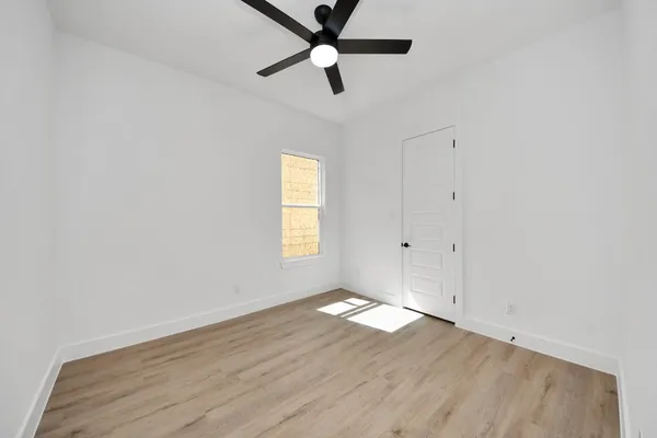 an empty room with wooden floor ceiling fan and windows