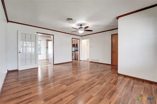 a view of an empty room with wooden floor and a ceiling fan