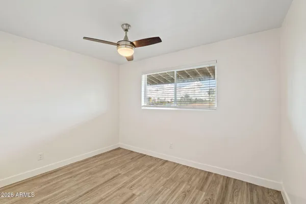 an empty room with wooden floor ceiling fan and window