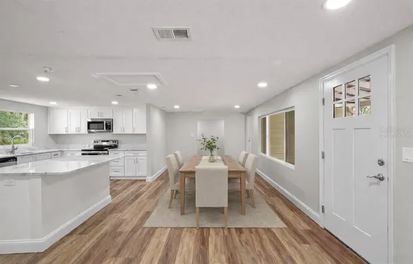 a large white kitchen with wooden floor and stainless steel appliances