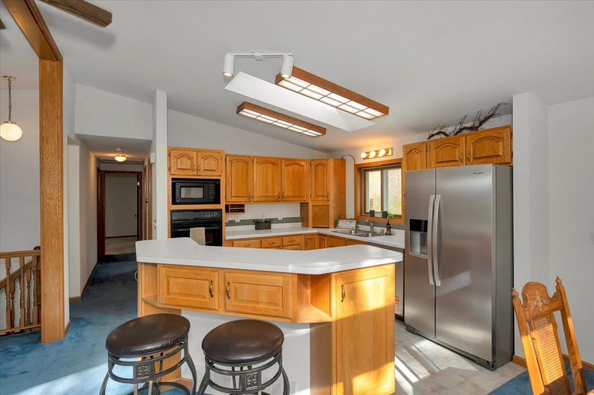 6373 Maple Grove Road Cloquet, MN 55720 - Photo 7 of 42 Kitchen with black appliances, vaulted ceiling, light countertops, a breakfast bar area, and a kitchen island