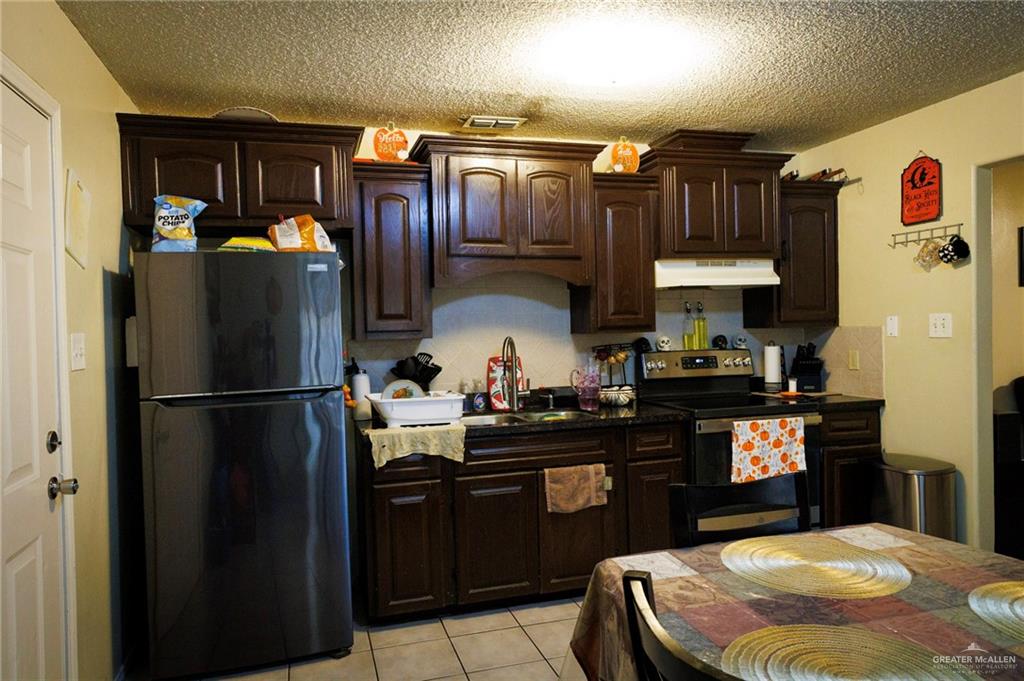 808 West Starr Avenue Pharr, TX 78577 - Photo 5 of 18 Kitchen with dark brown cabinetry, freestanding refrigerator, stainless steel range with electric stovetop, light tile patterned floors, and a textured ceiling