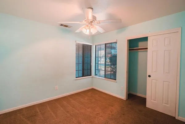 an empty room with chandelier fan and windows