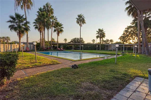 a view of a swimming pool with a yard and palm trees