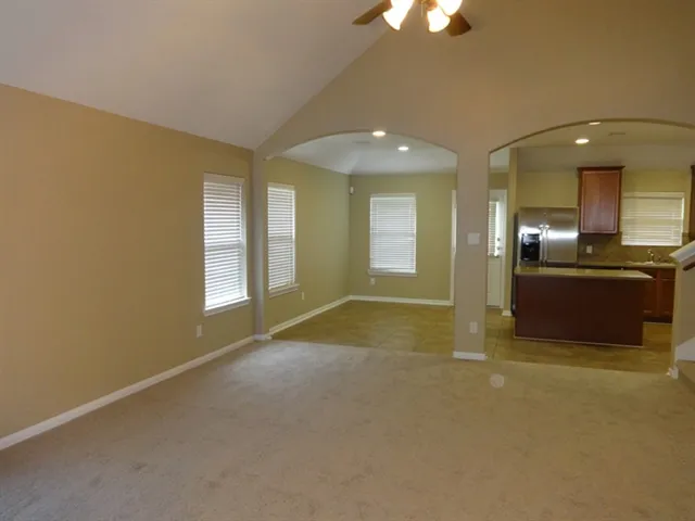 an empty room with a open kitchen and chandelier fan