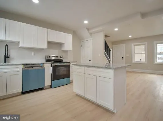 a kitchen with stainless steel appliances granite countertop a refrigerator a stove a sink and white cabinets