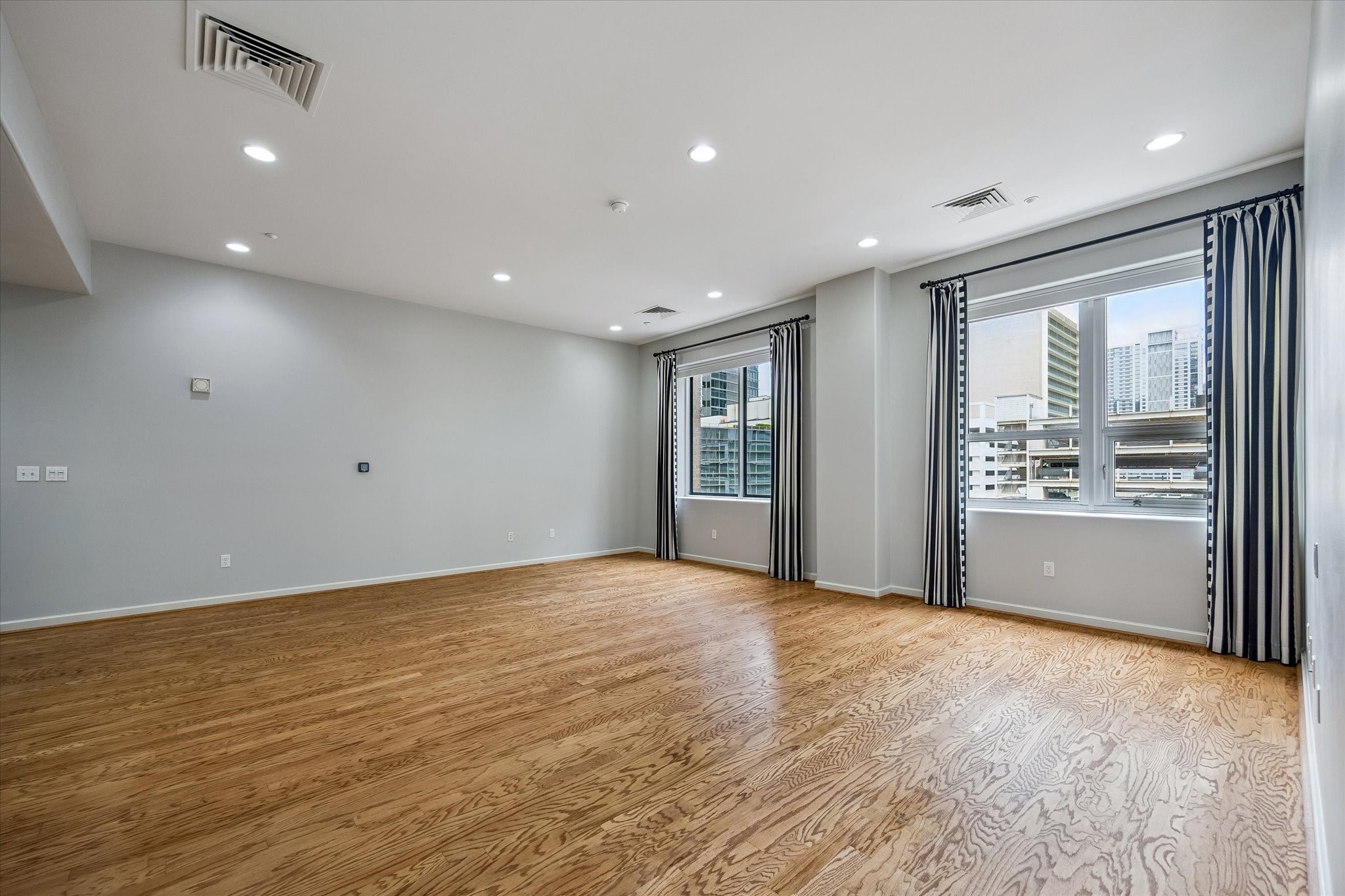 914 Main Street, Unit 910 Houston, TX 77002 - Photo 5 of 32 This spacious room features hardwood floors, neutral walls, and recessed lighting. Large windows with striped curtains provide ample natural light and offer a view of the cityscape. Perfect for a bright and open living area.