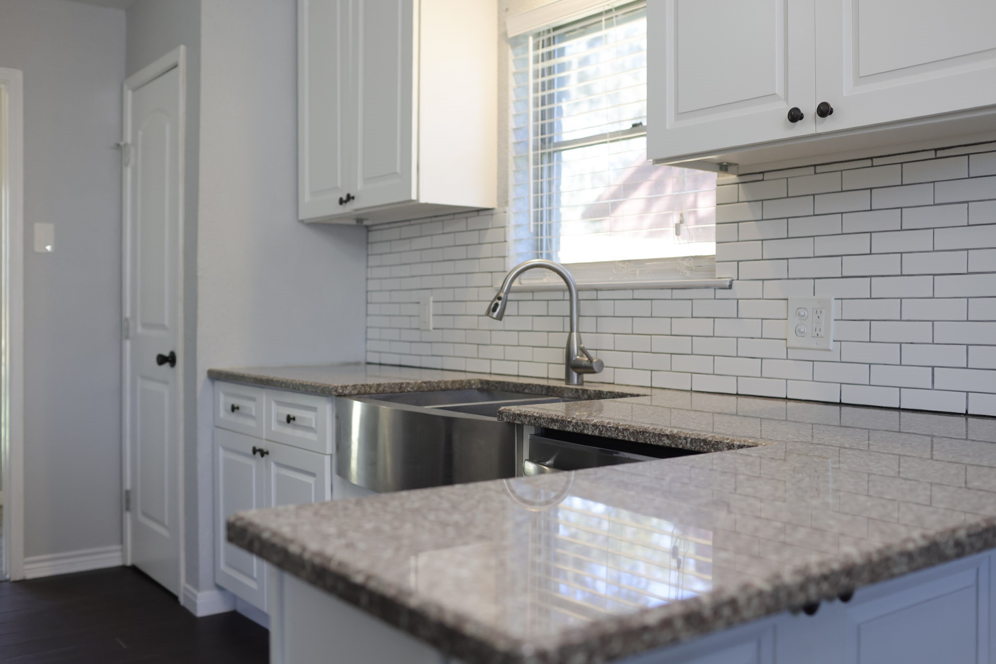 407 Tamarind Street Lake Jackson, TX 77566 - Photo 14 of 36 Modern kitchen with white cabinets, granite countertops, and a sleek stainless steel sink. The subway tile backsplash adds a stylish touch, and ample natural light streams through the window.