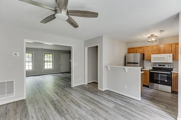 a view of a kitchen and an empty room with wooden floor a ceiling fan