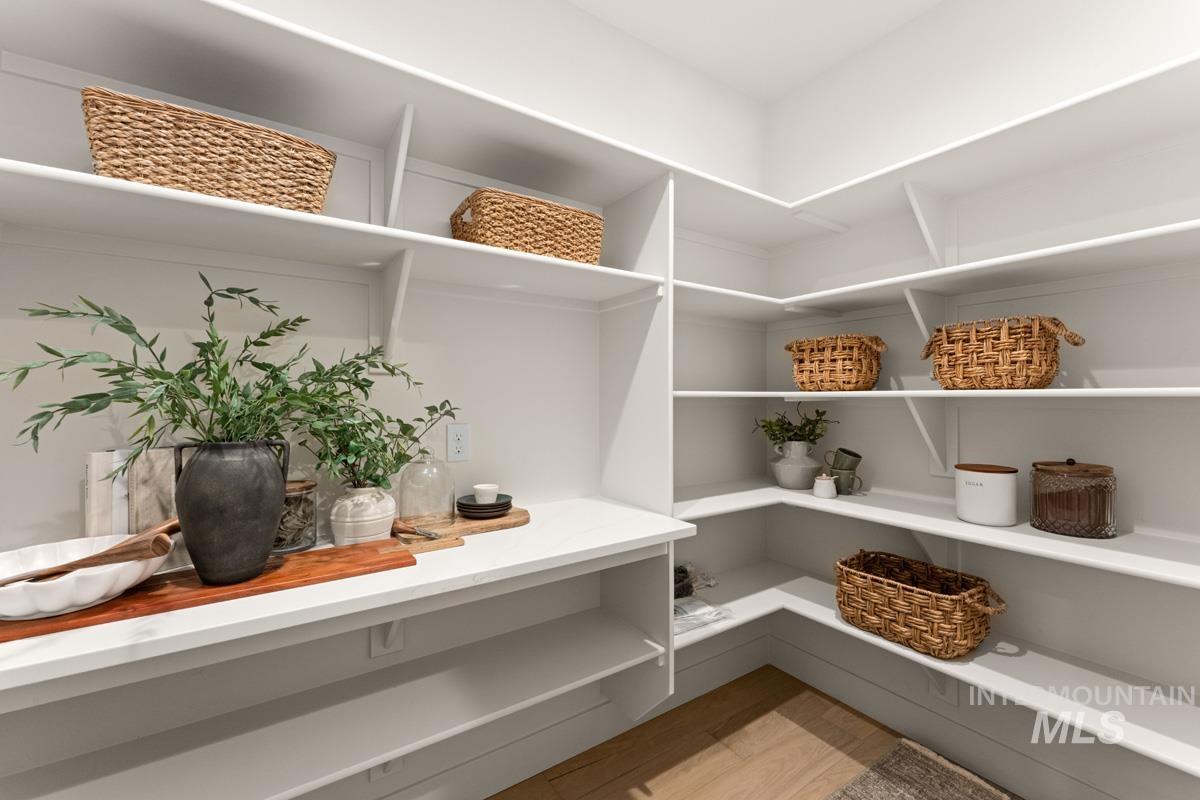 13338 North Spring Creek Way Boise, ID 83714 - Photo 11 of 46 Walk-in pantry featuring extensive built-in shelving, white finishes, corner storage, a countertop surface, and wood-finish flooring