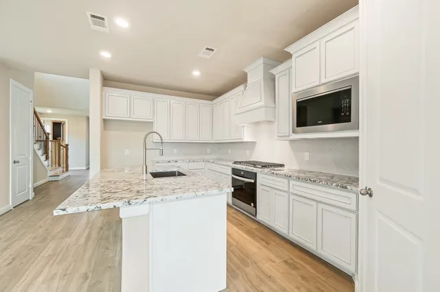 a kitchen with stainless steel appliances granite countertop a stove top oven a sink a refrigerator and white cabinets with wooden floor