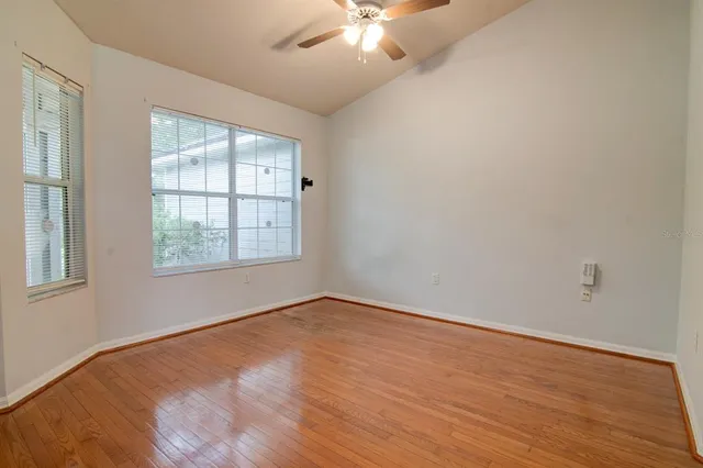 an empty room with wooden floor chandelier fan and windows