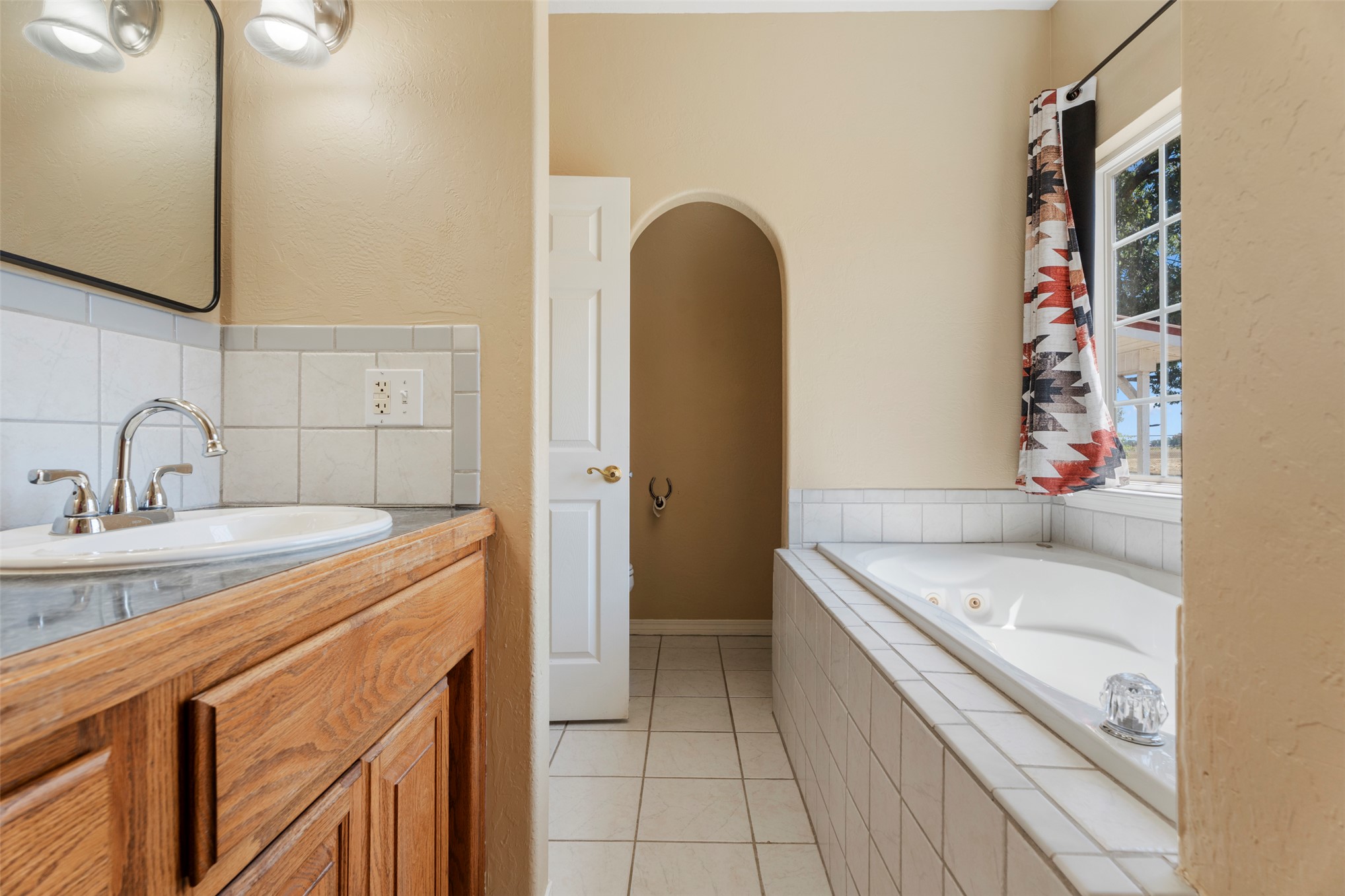 20233 East 570 Road Colcord, OK 74338 - Photo 22 of 39 Built-in soaking tub with tile surround, wood-finish vanity with an integrated sink, and tile flooring