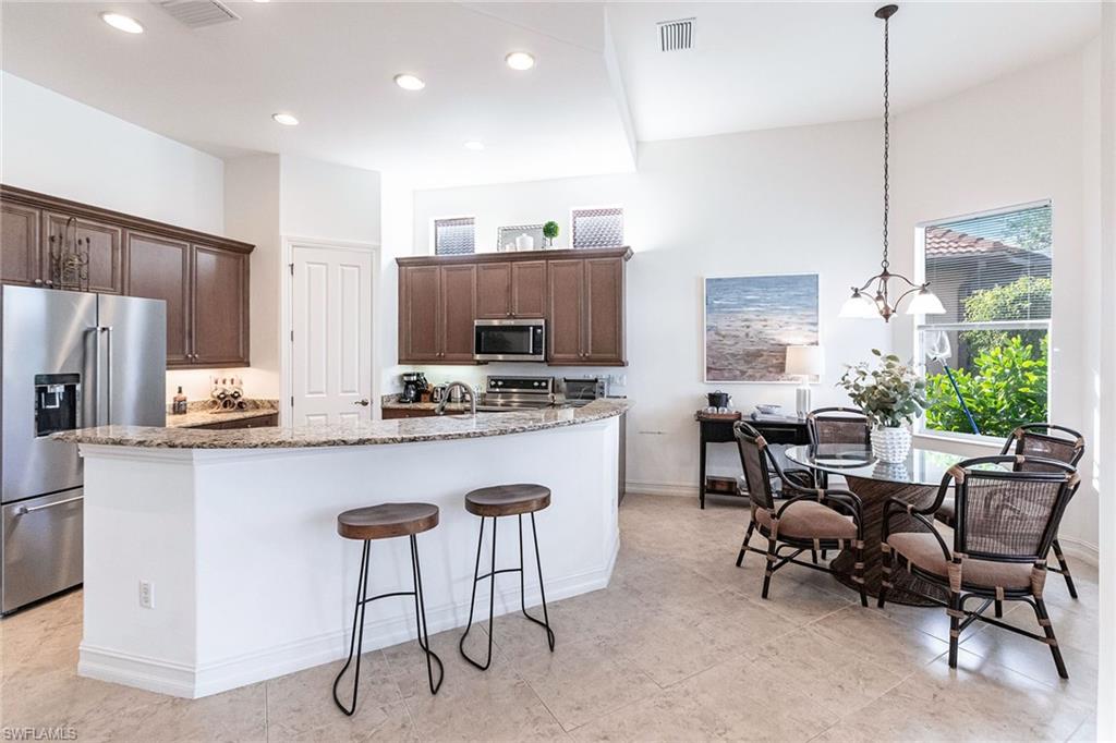 7863 Valencia Court Naples, FL 34113 - Photo 12 of 50 a kitchen with kitchen island granite countertop a table chairs stove a sink and a view of living room