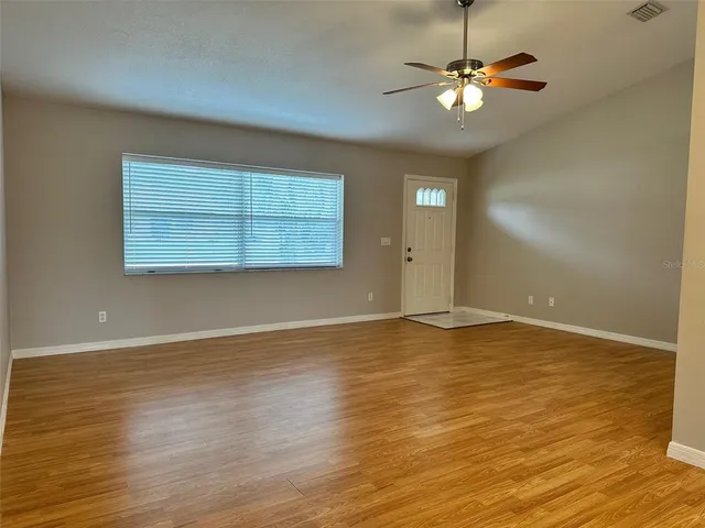 an empty room with wooden floor chandelier fan and windows