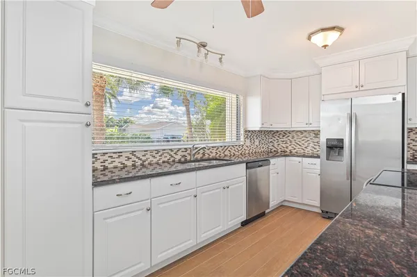 a kitchen with granite countertop white cabinets white appliances a sink and a large window