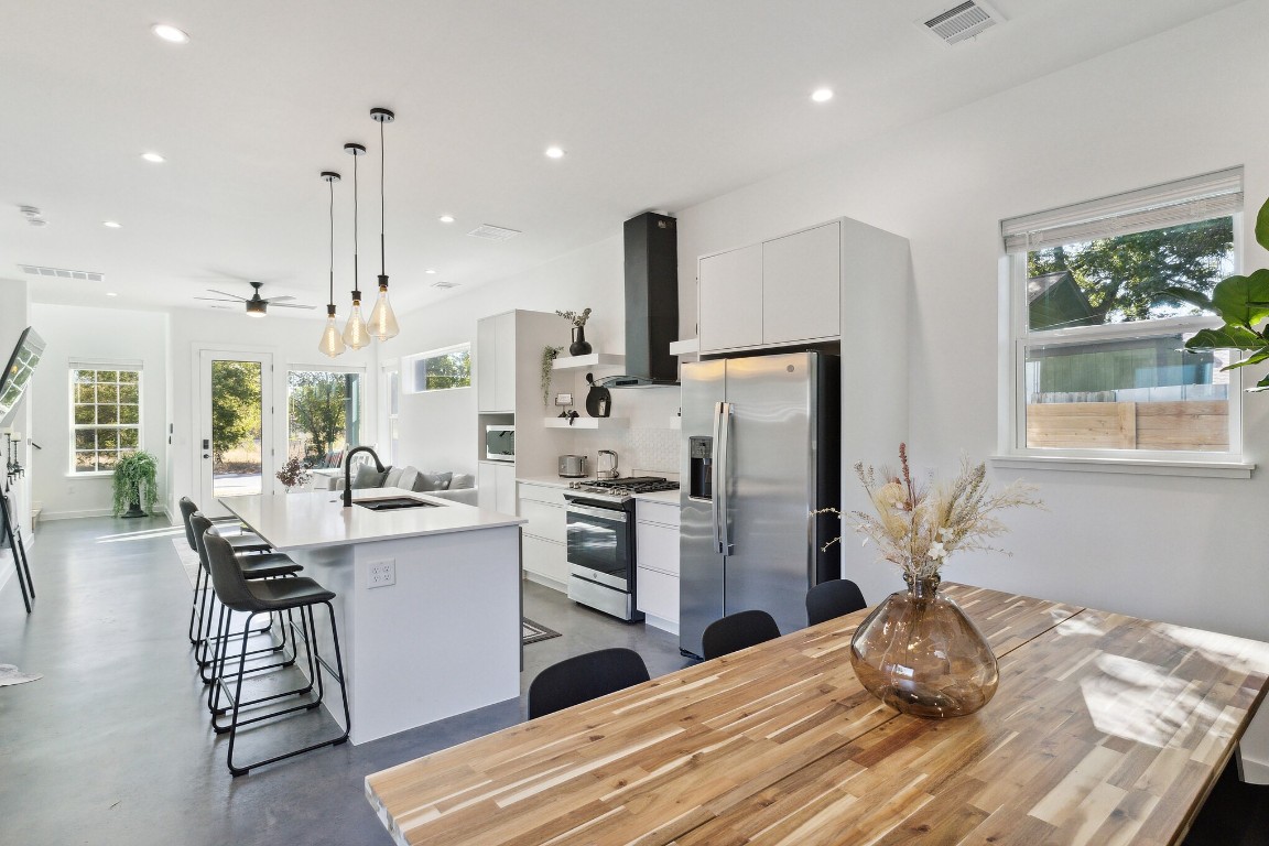 a kitchen with stainless steel appliances kitchen island granite countertop a refrigerator oven a sink dishwasher and a dining table with wooden floor