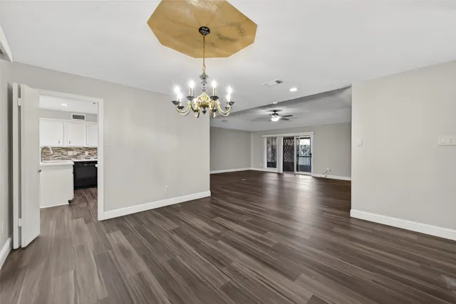 a view of a livingroom with wooden floor a ceiling fan and kitchen space