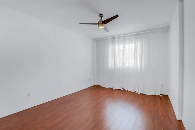 an empty room with wooden floor fan and windows