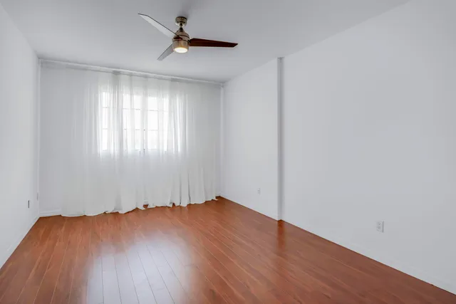 an empty room with wooden floor chandelier fan and windows