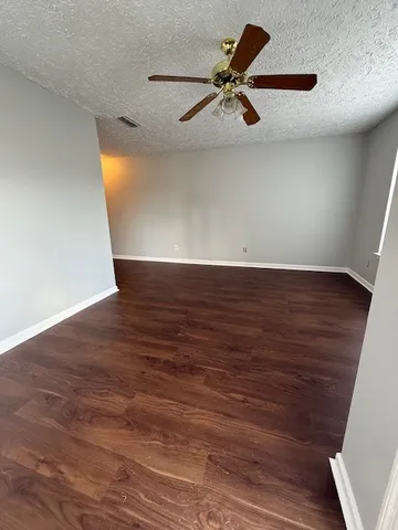 an empty room with wooden floor fan and windows