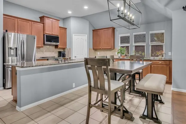 a kitchen with granite countertop stainless steel appliances a table chairs microwave and refrigerator