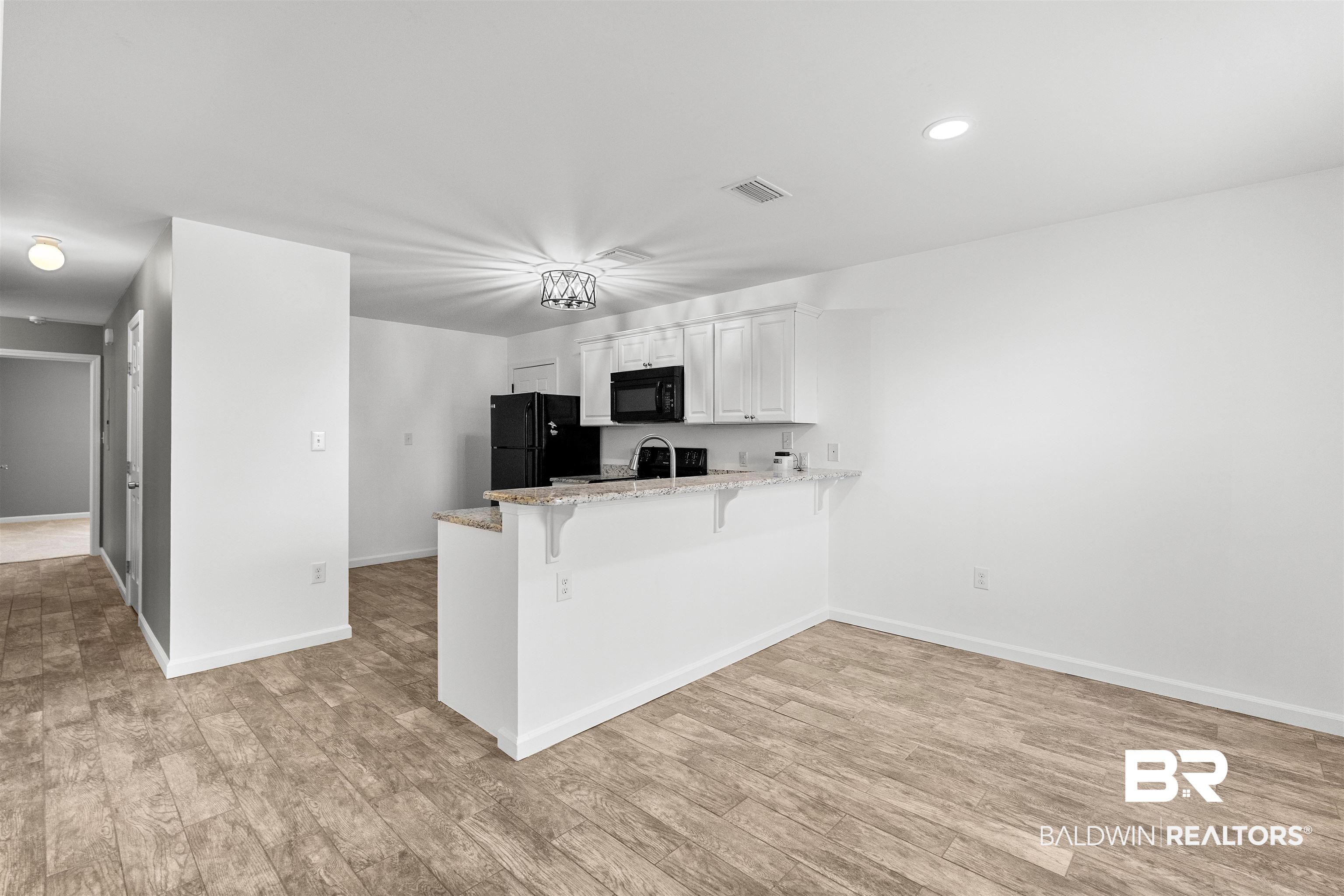 15131 Marem Drive Foley, AL 36535 - Photo 2 of 13 Kitchen with a kitchen breakfast bar, a peninsula, white cabinetry, light stone counters, and black appliances