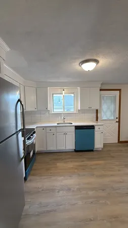 a large kitchen with a stove a sink dishwasher a refrigerator and white cabinets with wooden floor