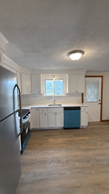 83 Pemberton Street, Unit A Revere, MA 02151 - Photo 3 of 13 a large kitchen with a stove a sink dishwasher a refrigerator and white cabinets with wooden floor