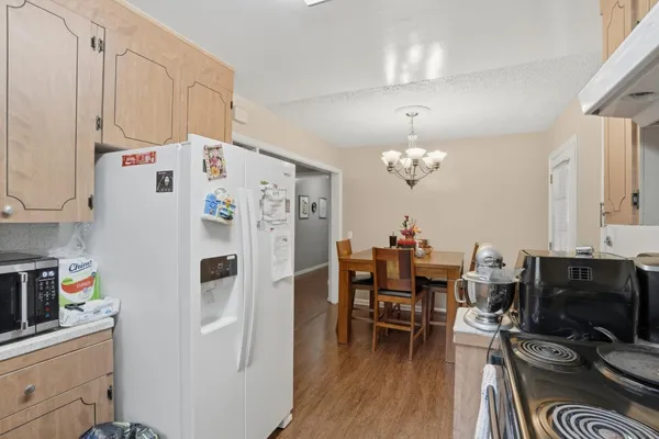 a white kitchen with stainless steel appliances a stove a refrigerator a dining table and chairs with wooden floor