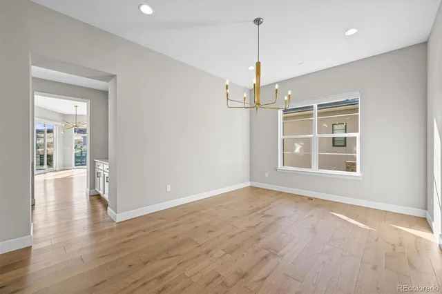 a view of an empty room with wooden floor kitchen view and a window