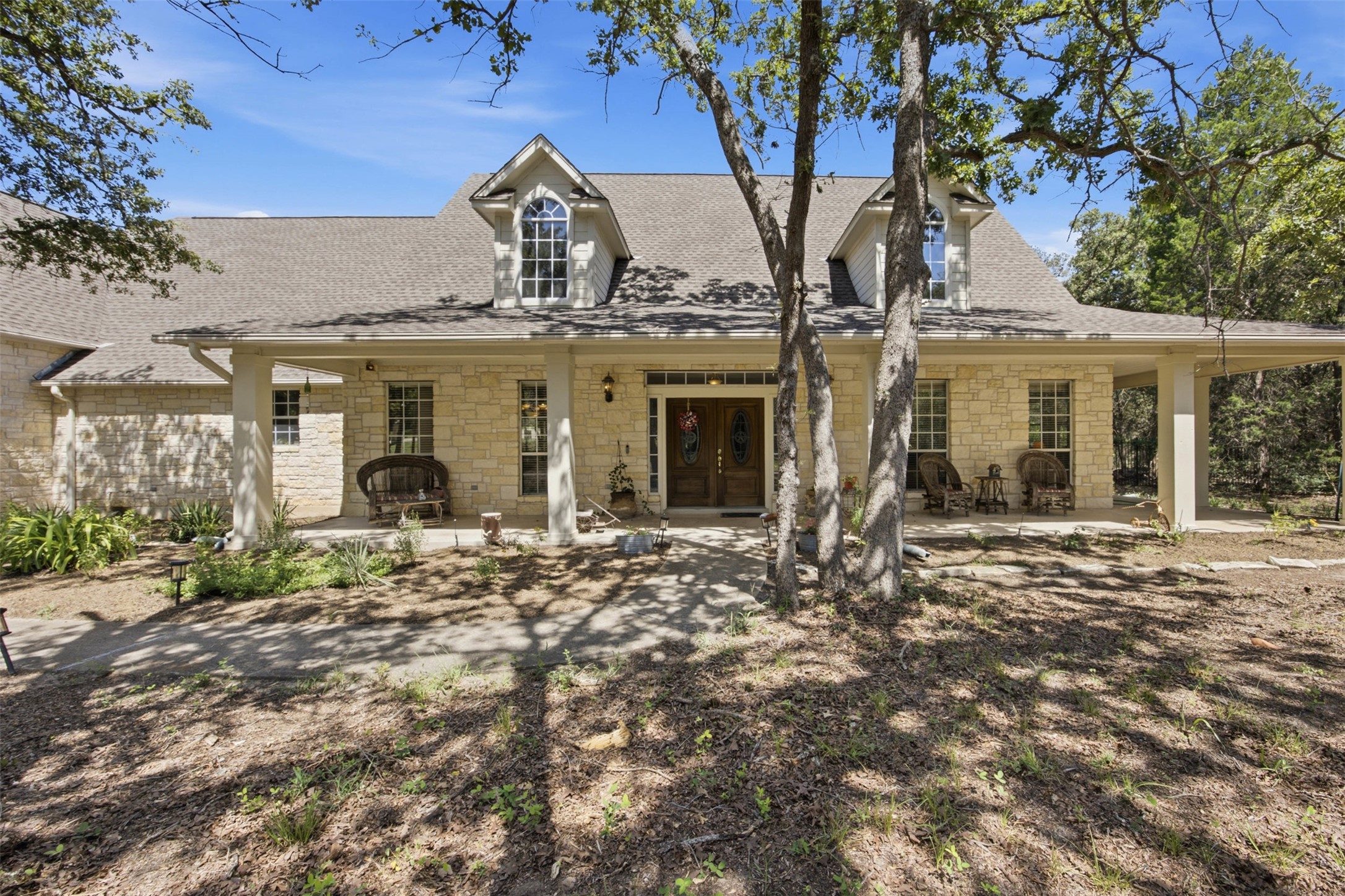 197 Elm Wood Drive Elgin, TX 78621 - Photo 11 of 37 A stone-clad home, featuring dormer windows and an inviting covered porch, nestles serenely amidst mature trees.