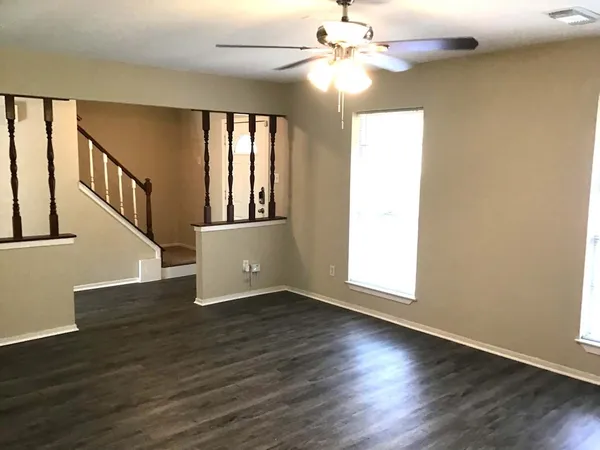 an empty room with wooden floor fan and windows
