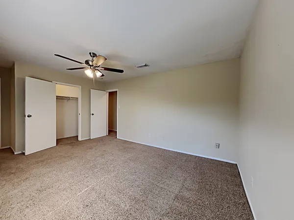 an empty room with a chandelier fan and windows