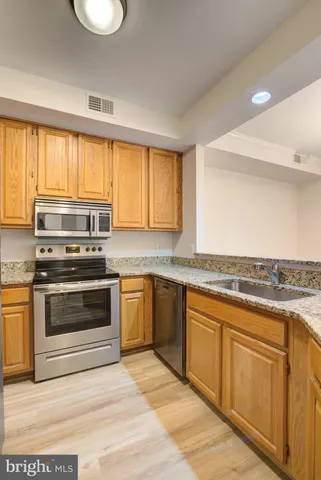 a kitchen with granite countertop a stove a sink and white cabinets with wooden floor