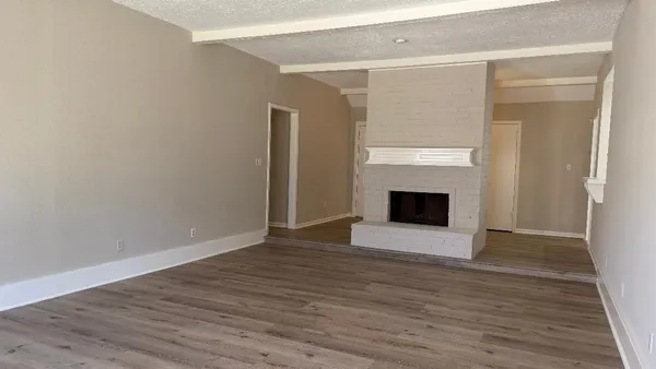 a view of an empty room with wooden floor and a fireplace