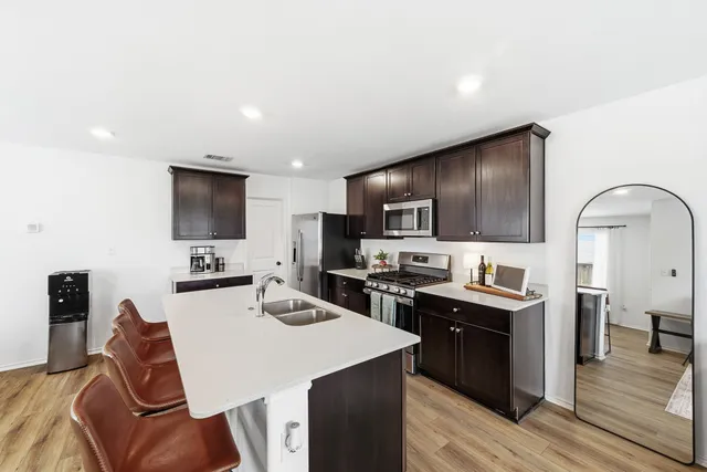 a kitchen with stainless steel appliances kitchen island granite countertop a sink dishwasher a stove top oven a refrigerator with island and chairs with wooden floor