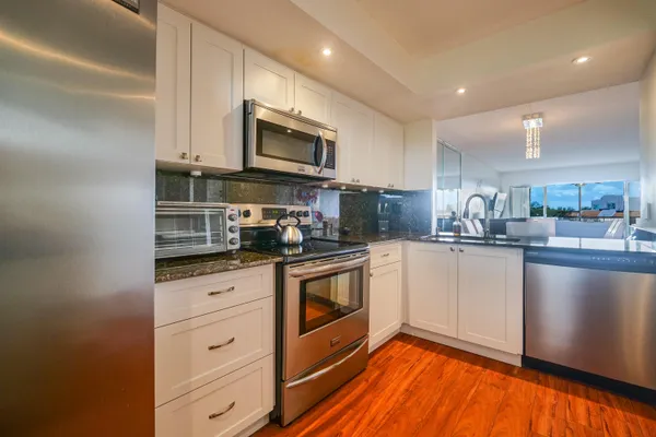 a kitchen with stainless steel appliances granite countertop a refrigerator a stove top oven a sink and dishwasher with wooden floor