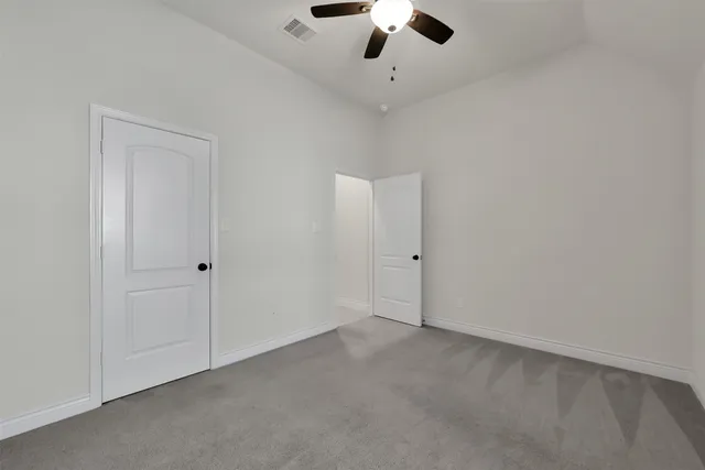 an empty room with a chandelier fan and kitchen view