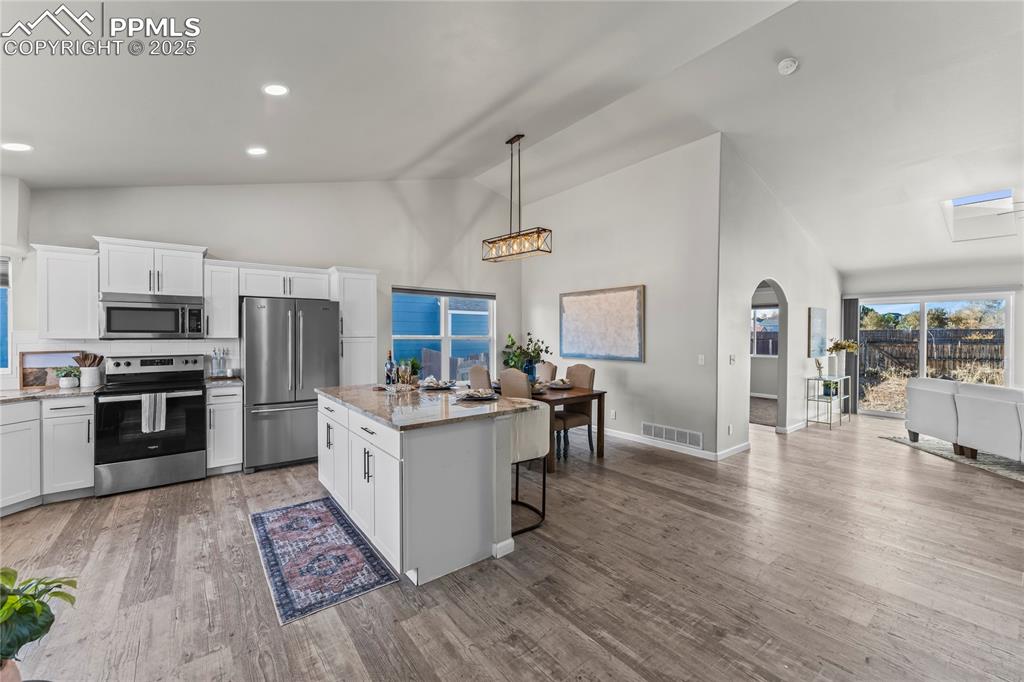 8168 Oliver Road Peyton, CO 80831 - Photo 7 of 42 a kitchen with stainless steel appliances a stove top oven a sink dishwasher a refrigerator and a dining table with wooden floor