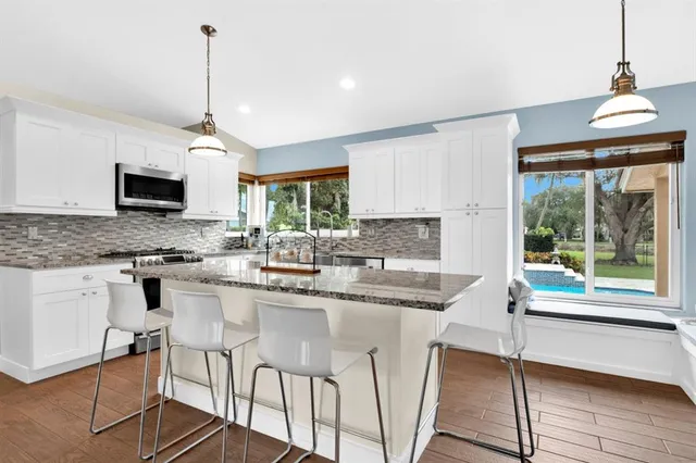 a kitchen with stainless steel appliances granite countertop a stove a sink dishwasher a refrigerator with a dining table and chairs with wooden floor