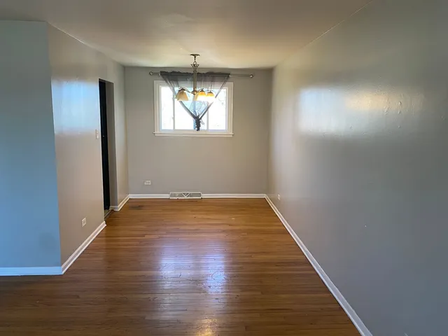 an empty room with wooden floor chandelier and windows