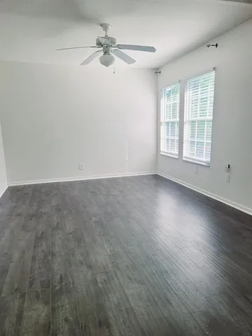 an empty room with wooden floor fan and windows