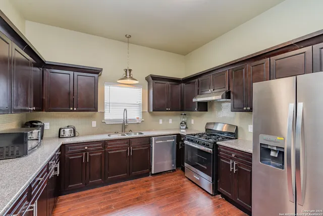 a kitchen with stainless steel appliances granite countertop a refrigerator a sink dishwasher a stove top oven a refrigerator with cabinets and wooden floor
