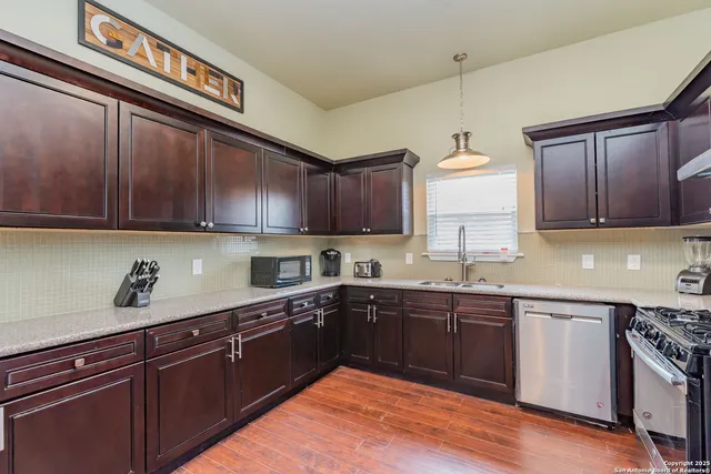 a kitchen with stainless steel appliances granite countertop wooden cabinets a stove top oven a sink and dishwasher with wooden floor