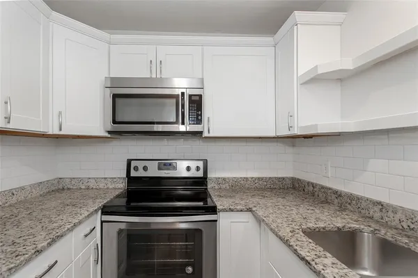 a kitchen with granite countertop white cabinets stainless steel appliances and a counter space