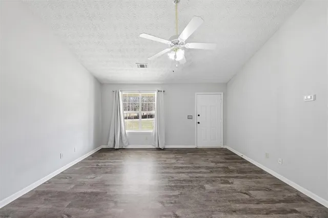 an empty room with wooden floor fan and windows