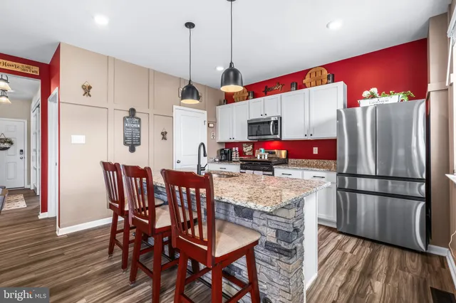 a kitchen with stainless steel appliances granite countertop a refrigerator a microwave oven a sink dishwasher and a dining table with wooden floor